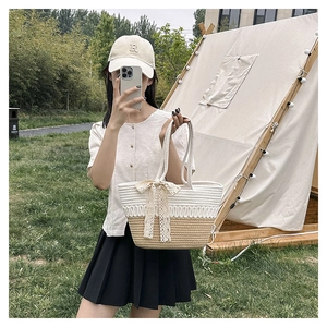 Detail of hand-woven straw tote with cream lace bow and dual-tone texture in outdoor setting