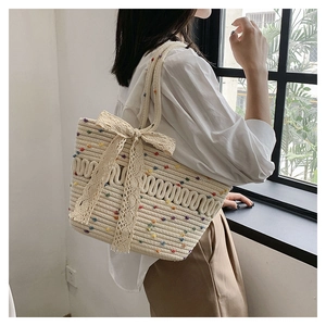 Detail of woven straw tote bag featuring colorful pom-poms and a large lace bow