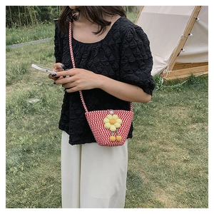 Detail of red and white checkered straw bag with a yellow plush sunflower charm