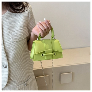 Detail of neon green mini crossbody bag with gold chain strap and top handle held by model