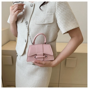 Sac trapèze minimaliste rose avec chaîne en métal porté sur une tenue en tweed
