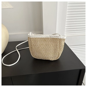 Detailed view of handmade woven straw bucket bag with white leather straps and trim