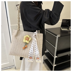 Detail of woven straw tote bag with braided handles, daisy charm and printed silk scarf