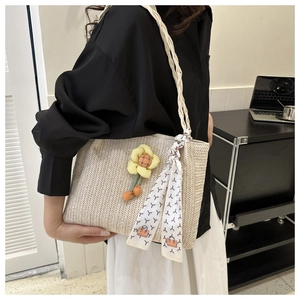 Detail of hand-woven straw tote bag with braided handles and floral charm accent