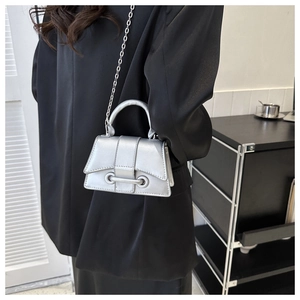 Silver mini crossbody bag with metal chain strap and top handle shown on black blazer