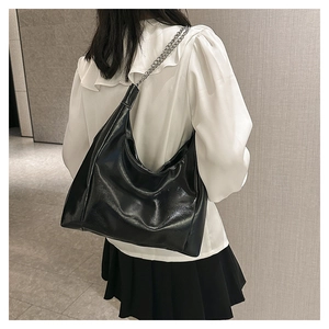 Détail d'un grand sac hobo noir brillant avec chaîne argentée porté par un mannequin
