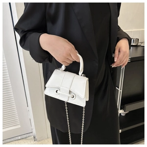 Detail of white leather mini handbag with silver chain strap on a black blazer