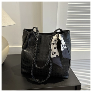 Detail of black tote bag featuring houndstooth texture and silk scarf on woven handle