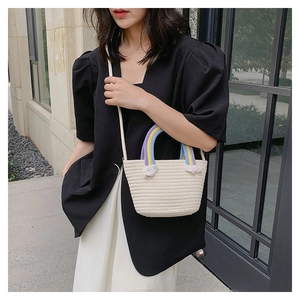 Detailaufnahme der beigen Strohtasche mit bunten Regenbogen-Griffen und weißen Fransen