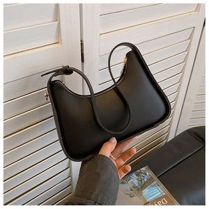 Close-up of black leather hobo bag with gold zipper and adjustable strap on white wood