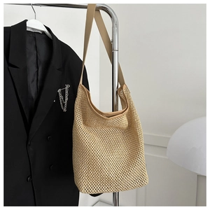 Détail du sac cabas en paille tissée avec bandoulière en cuir suspendu sur un support