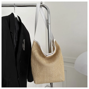 Gros plan d'un sac cabas en paille tissée avec bandoulière en cuir blanc sur un cintre minimaliste