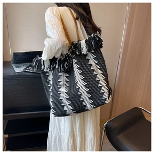Detail of woven tote bag with geometric pattern and long black and white tassels