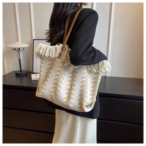 Detail of knit tote bag with fringes and brown leather straps on model's shoulder