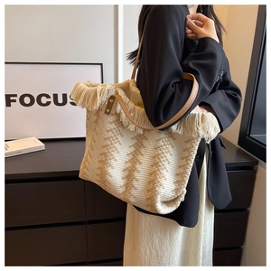 Detail of woven tote bag featuring beige geometric patterns and cream tassel accents