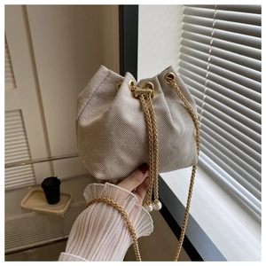 Détail d'un sac seau tissé crème avec bandoulière chaîne dorée et cordon en perles