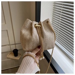 Détail du sac seau tissé avec cordon en perles et bandoulière chaîne dorée pour femme
