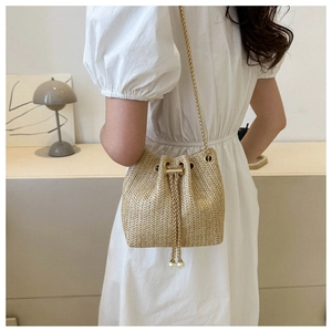 Détail du sac seau en paille tressée avec bandoulière dorée et accents de perles