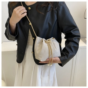 Gros plan d'un sac seau blanc tressé avec chaîne dorée et détails de perles sur le cordon