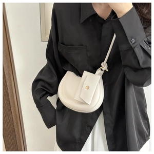 Detail of white half-moon bag featuring a decorative knot strap and hanging card pouch