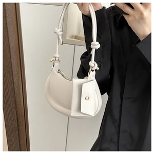 Close-up of white half-moon shoulder bag with decorative knotted strap and mini pouch