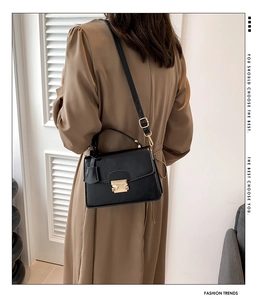 Detail van een zwarte leren crossbodytas met gouden gesp gedragen door een model