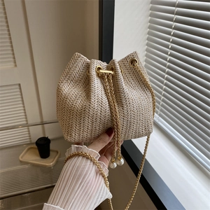 Sac seau tissé beige chic avec chaîne dorée et cordon perlé tenu à la main
