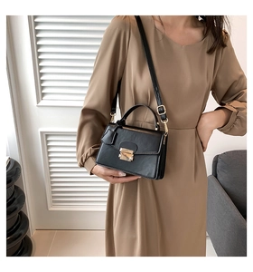 Detail van zwarte crossbody tas met gouden gesp en lederen handvat aan de bovenkant