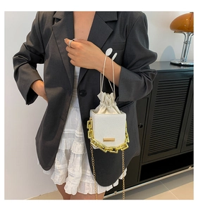 Close-up of white mini square box bag featuring chunky gold chain and drawstring pouch