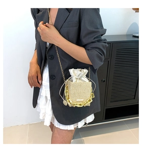 Detail of a woven straw crossbody bag featuring golden chain and drawstring inner