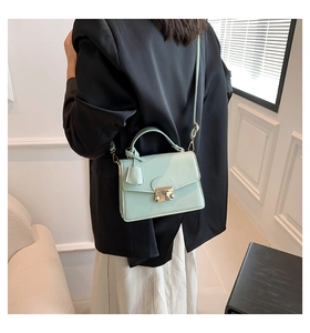Model draagt een muntgroene crossbodytas met metalen sluiting over een zwart pak