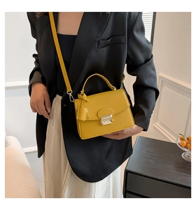 Detail van een felgele mini-crossbodytas met een zilveren metalen sluiting en handvat