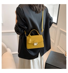 Detail van gele lederen crossbodytas met metalen slot gedragen door een model in pak