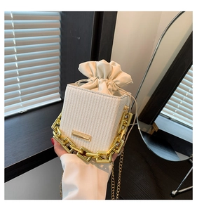 Detail of white woven bucket bag with thick gold chain handle and drawstring closure
