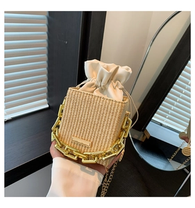 Detail of woven straw bucket bag with white drawstring closure and chunky gold chain handle
