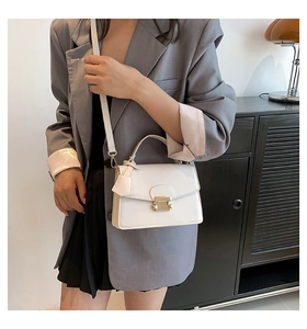 Chique witte kleine vierkante tas met gouden trapeziumslot gedragen door een model in grijs