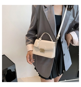 Detail van een gebroken witte handtas met gouden sluiting gedragen met een grijze blazer