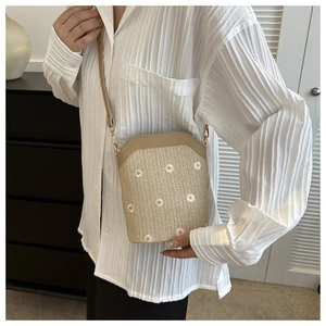 Détail de broderie marguerite sur un sac bandoulière en paille porté par un mannequin