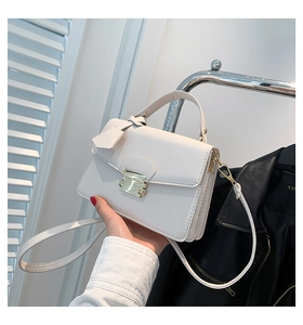 Detail van witte kunstlederen crossbodytas met vierkante gouden gesp en handvat bovenop