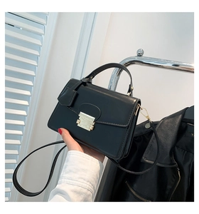 Detail van zwarte PU-leren crossbodytas met gouden vierkant slot en handvat aan de bovenkant