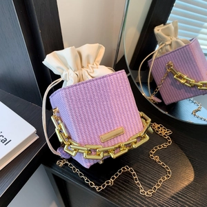 Fashionable purple woven chain handbag with white drawstring liner on wood surface