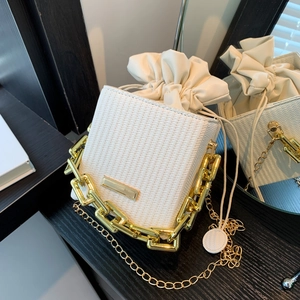 White woven bucket bag with gold chain strap and drawstring closure on black wood