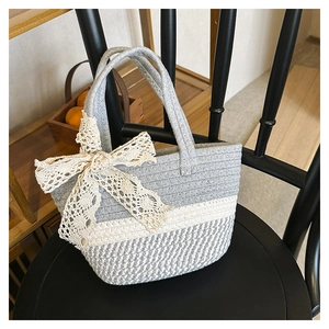 Detail of hand-woven straw bucket bag featuring a cream lace bow on a textured surface