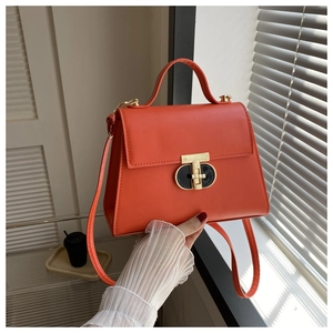 Close-up of orange trapezoid PU leather handbag with golden twist lock and top handle