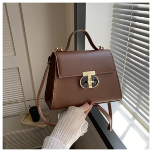 Close-up of caramel leather handbag with gold T-shaped clasp and natural sunlight shadows