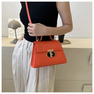 Detail of coral orange PU leather handbag with gold T-shaped clasp on a fashion model