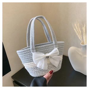 Detail of hand-woven straw bag featuring a large mesh bow and grey-white color contrast
