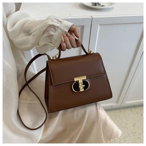 Detailed shot of brown trapezoid handbag with gold T-shaped lock and long strap