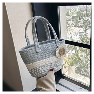 Detail of hand-woven striped beach bag with white daisy charm and round handles