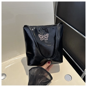 Close-up of black patent leather tote bag with a pink butterfly embroidery detail
